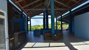 Un espace extérieur abrité, doté d’un sol carrelé, de piliers bleus et de mobilier en osier.