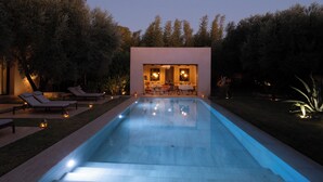 Un espace piscine extérieur moderne, doté de chaises longues et d’un coin repas visible à travers une porte ouverte.