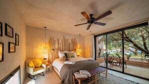 Une chambre à coucher moderne, dotée d’un grand lit, d’un ventilateur de plafond et offrant une vue sur l’extérieur grâce à de grandes fenêtres.