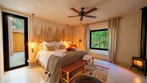 Une chambre à coucher comprenant un lit, des lampes de chevet, un banc, une fenêtre avec vue, un ventilateur de plafond et un poêle à bois.