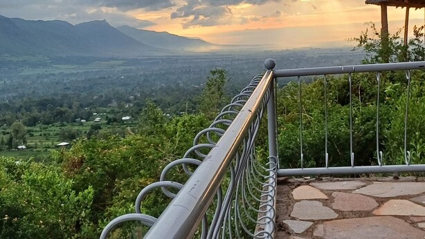A metal railing overlooking a valley with a stone pathway and a gazebo. - Hillbilly Bush Lodge  (Kisumu)