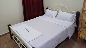 A neatly made bed with white linens and pillows, a wooden headboard, and a wooden ladder against the wall. - Hillbilly Bush Lodge  (Kisumu)
