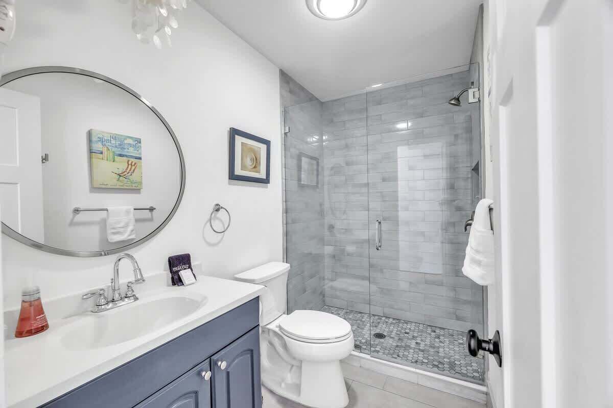 A bathroom with a white sink, a mirror, a toilet, and a glass shower enclosure.