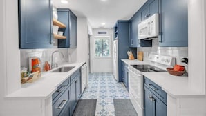 Une cuisine étroite avec des meubles bleus, des plans de travail blancs et des carreaux de sol à motifs.