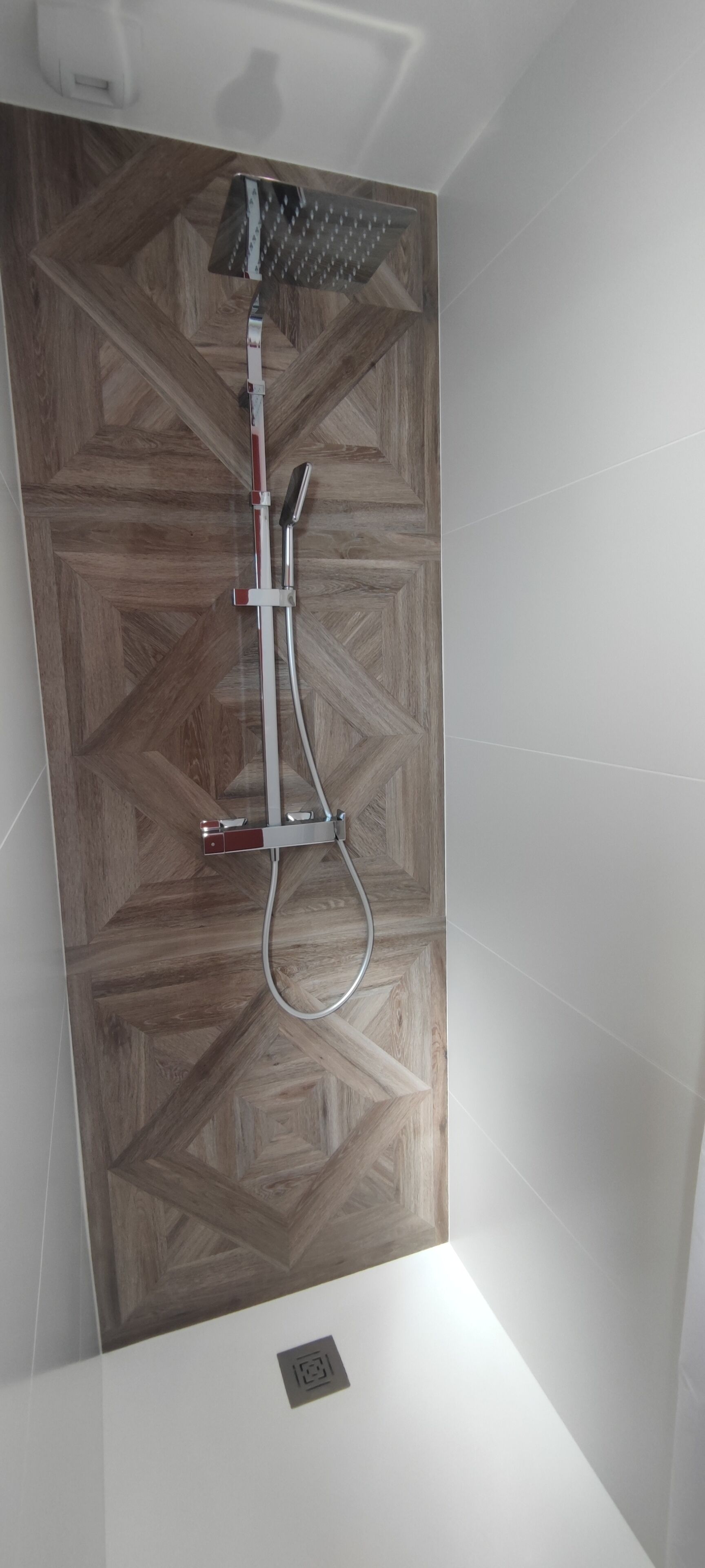 A shower with a wooden panel wall and a handheld showerhead.