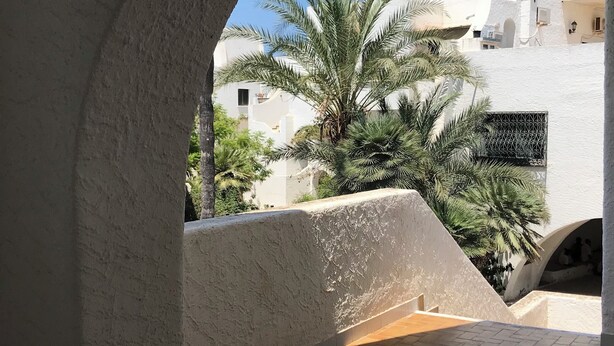 An arched architectural feature with a view of a white building and palm trees.