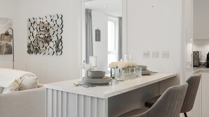 Ένας μοντέρνος χώρος τραπεζαρίας με έναν λευκό μαρμάρινο πάγκο, έναν μεγάλο καθρέφτη και ένα διακοσμητικό στοιχείο στον τοίχο.