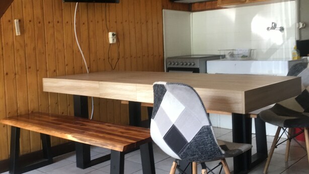 A kitchen with wooden cabinets, a wooden dining table, a bench, and a chair with a checkered pattern.