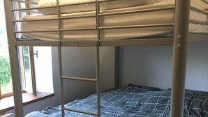 A bunk bed with a checkered bedspread and pillows, a window with a view of greenery, and a tiled floor.