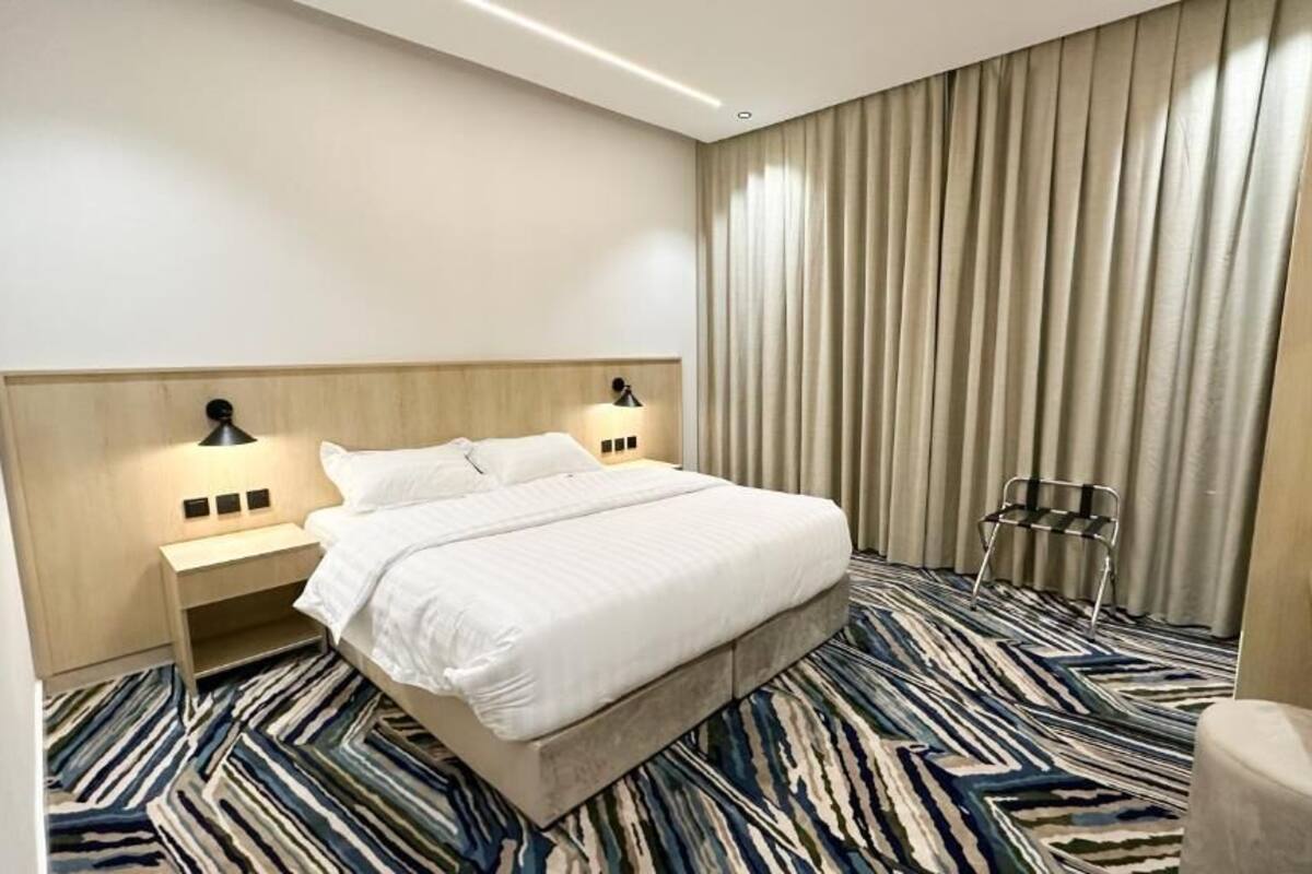 A hotel room with a large bed, a nightstand with a lamp, a chair, and a desk.