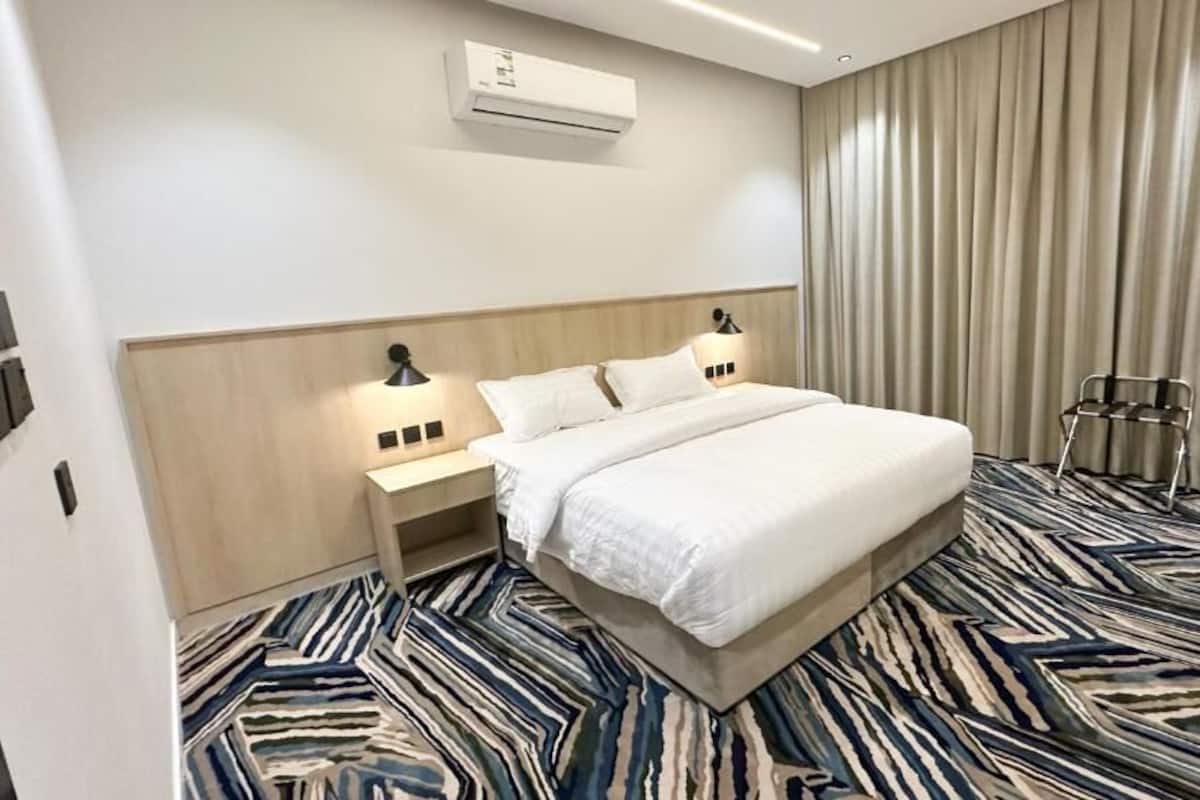 A hotel room with a bed, bedside tables, a lamp, a chair, and a patterned carpet.