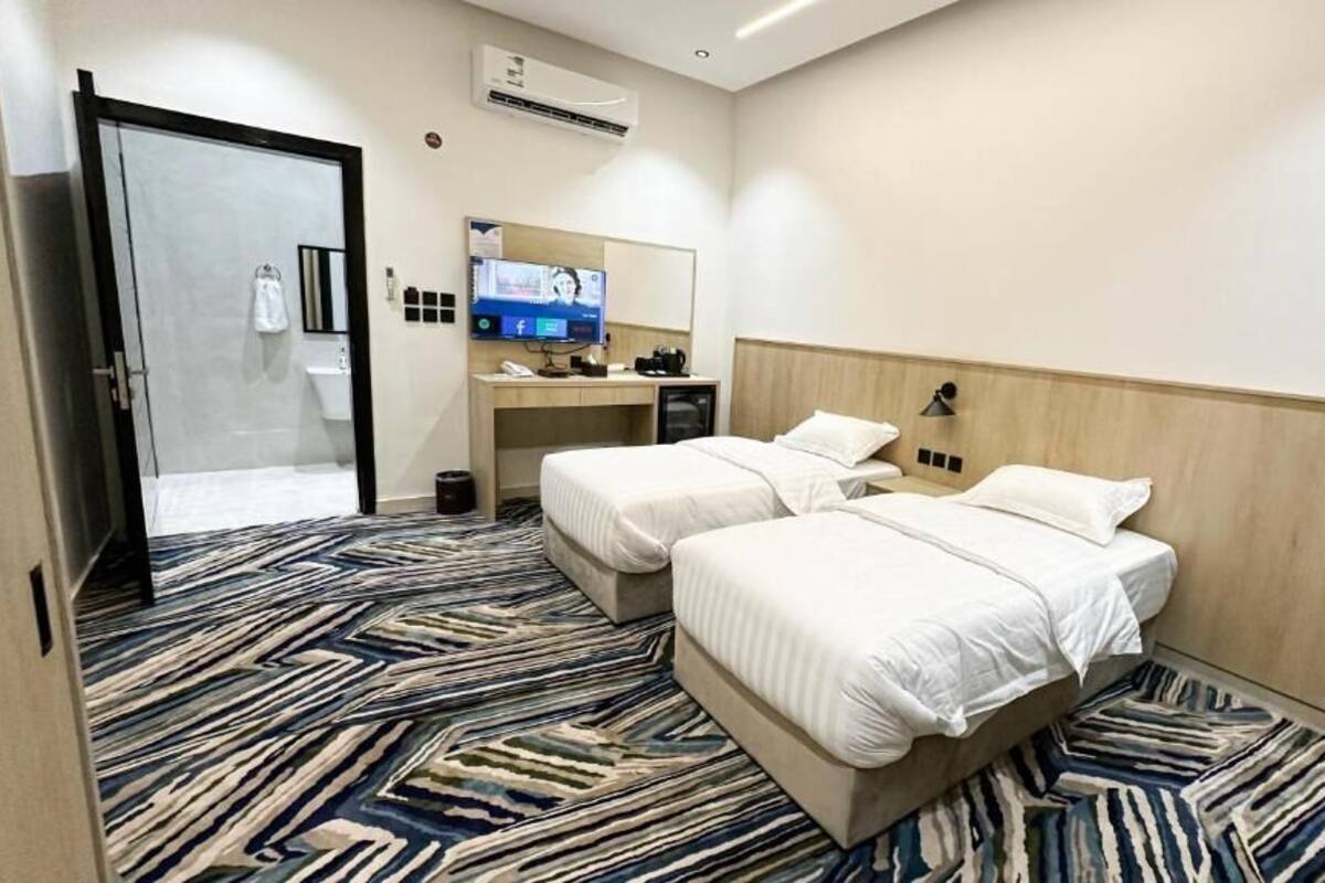 A hotel room with two beds, a desk, a TV, and a shower area.