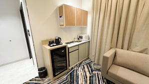 Une chambre d’hôtel compacte comprenant un coin cuisine, un canapé et un tapis à motifs.