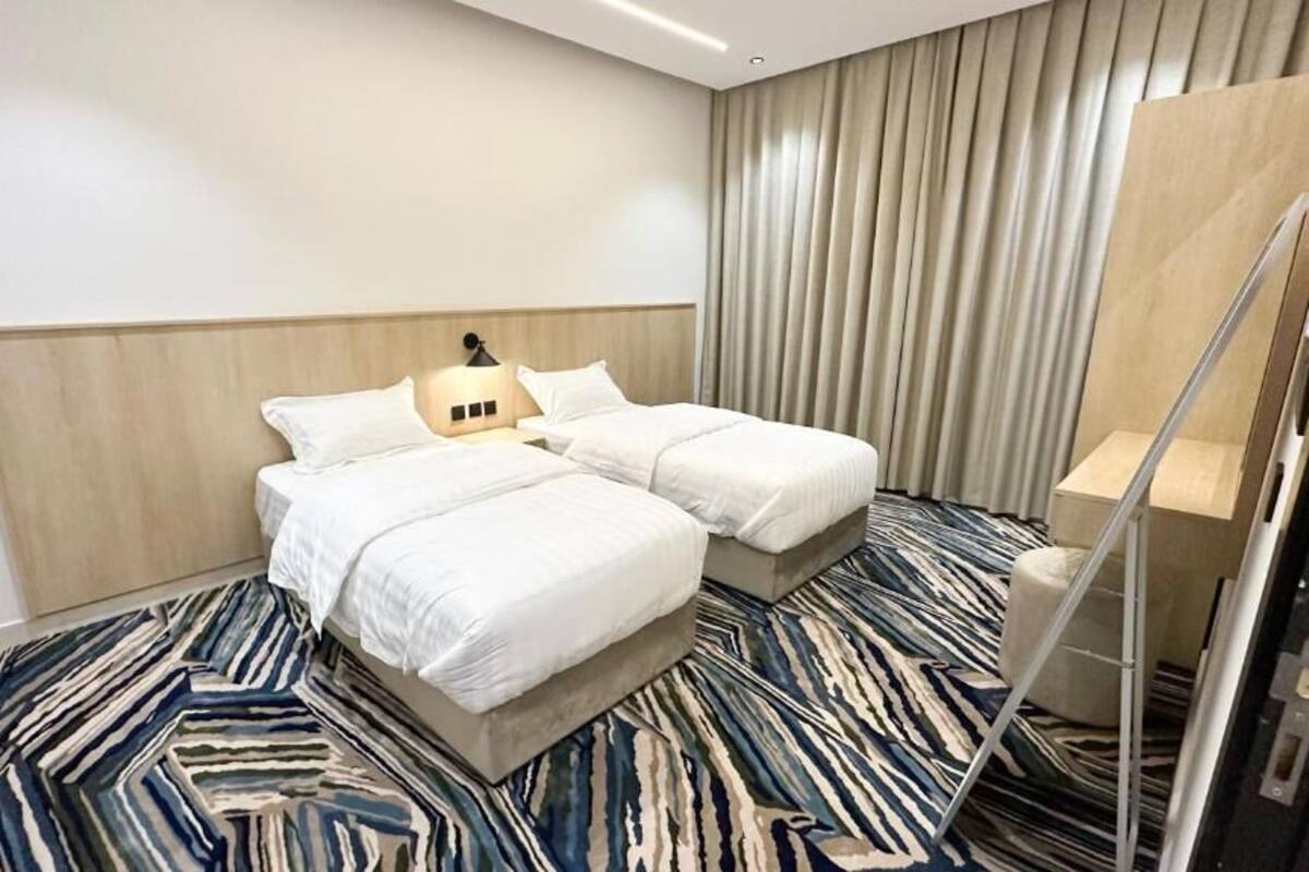 A hotel room with two beds, a wooden headboard, a striped carpet, and a large window with curtains.