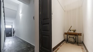 Egy sötétfa ajtóval rendelkező folyosó, egy kis asztalon egy varrógép, és a padlón egy mintás szőnyeg.