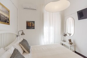 Un dormitorio con cama, mesita de noche con lámpara, espejo e imagen en la pared.