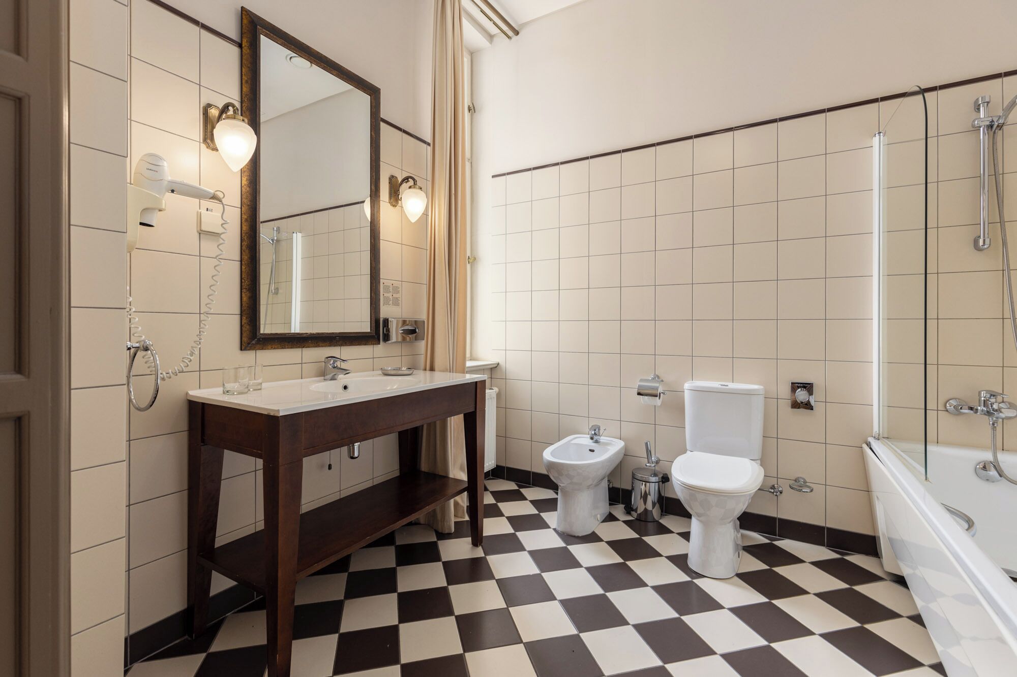 A bathroom with a checkered floor, a double sink vanity, a toilet, and a bathtub.