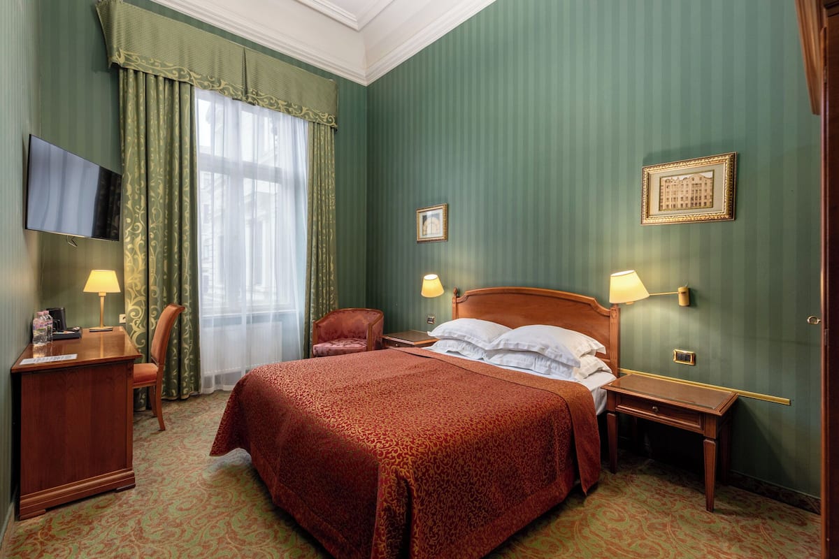 A hotel room with a large bed, two bedside tables, a desk with a chair, a TV, and green walls.