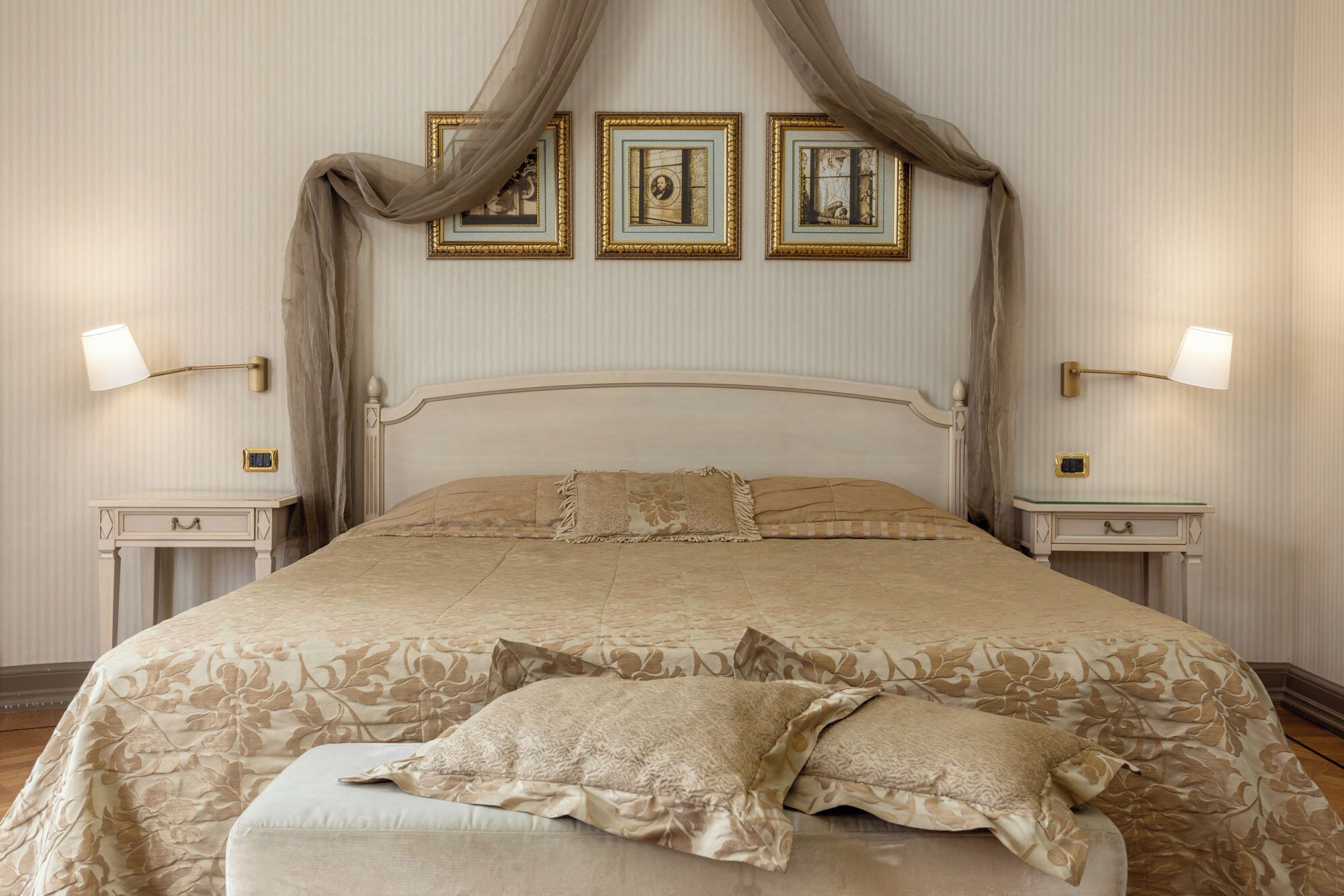 A four-poster bed with a floral bedspread, two bedside lamps, and three framed pictures on the wall.