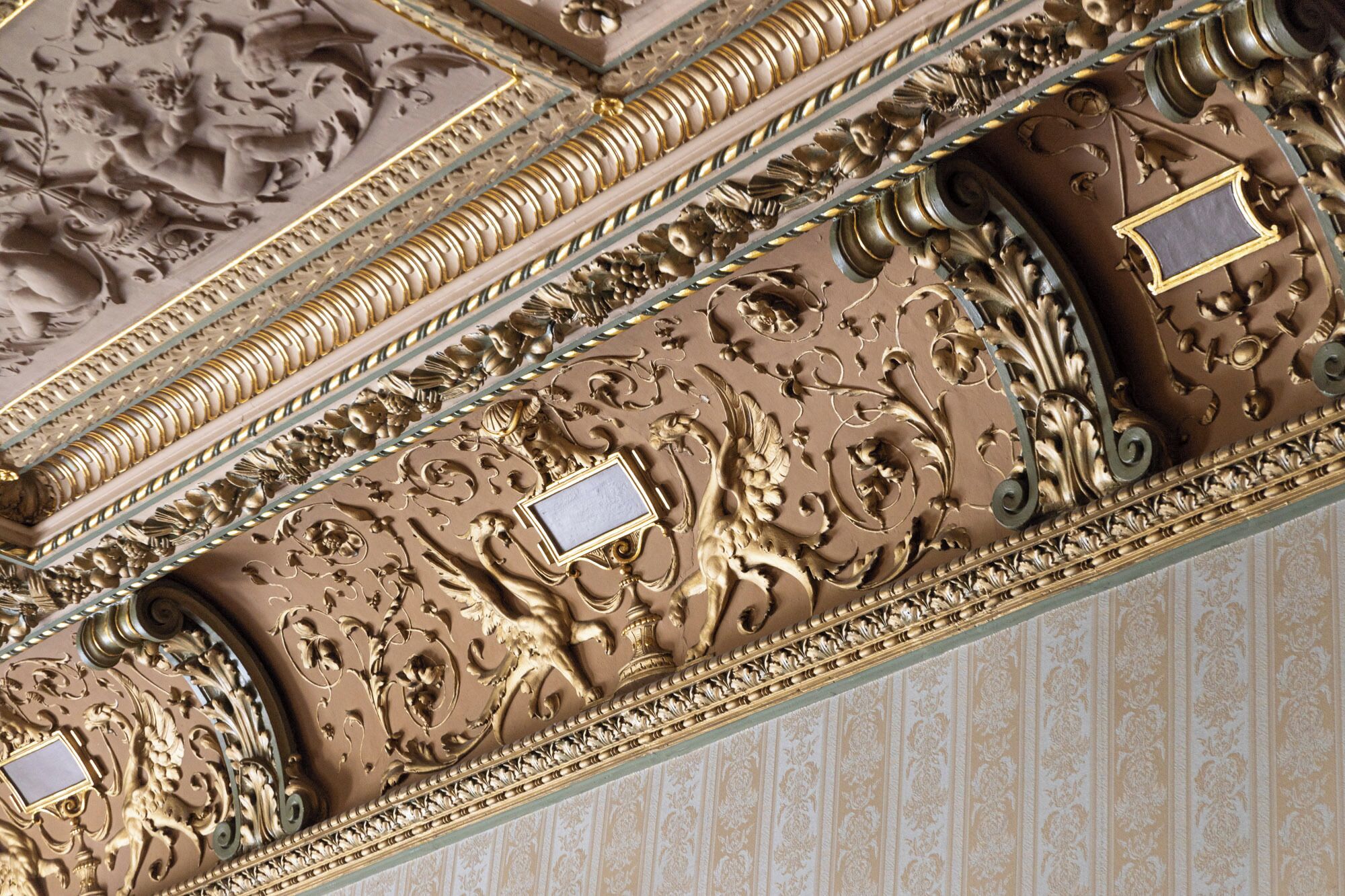 Un techo detallado con ornamentos dorados y marrones, que incluyen motivos florales y una medalla central.