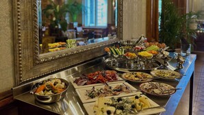 Une table de buffet garnie de divers plats, un grand miroir décoratif et un lustre dans une pièce aux murs lambrissés et au plafond haut.