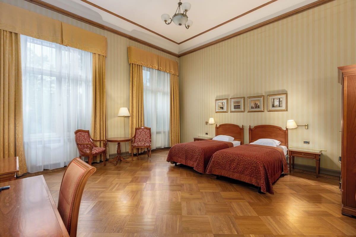 A hotel room with two beds, a sitting area with a chair and table, and a large window with curtains.