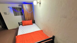 A single bed with an orange bedspread and a white pillow in a room with a wooden wardrobe, a light fixture, and a wall-mounted light. - Professional Lahore Hostels (Lahore)