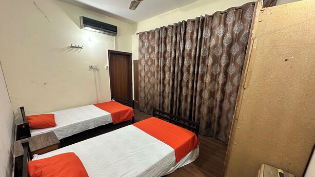 A room with two beds, a ceiling fan, an air conditioning unit, and a curtain. - Professional Lahore Hostels (Lahore)