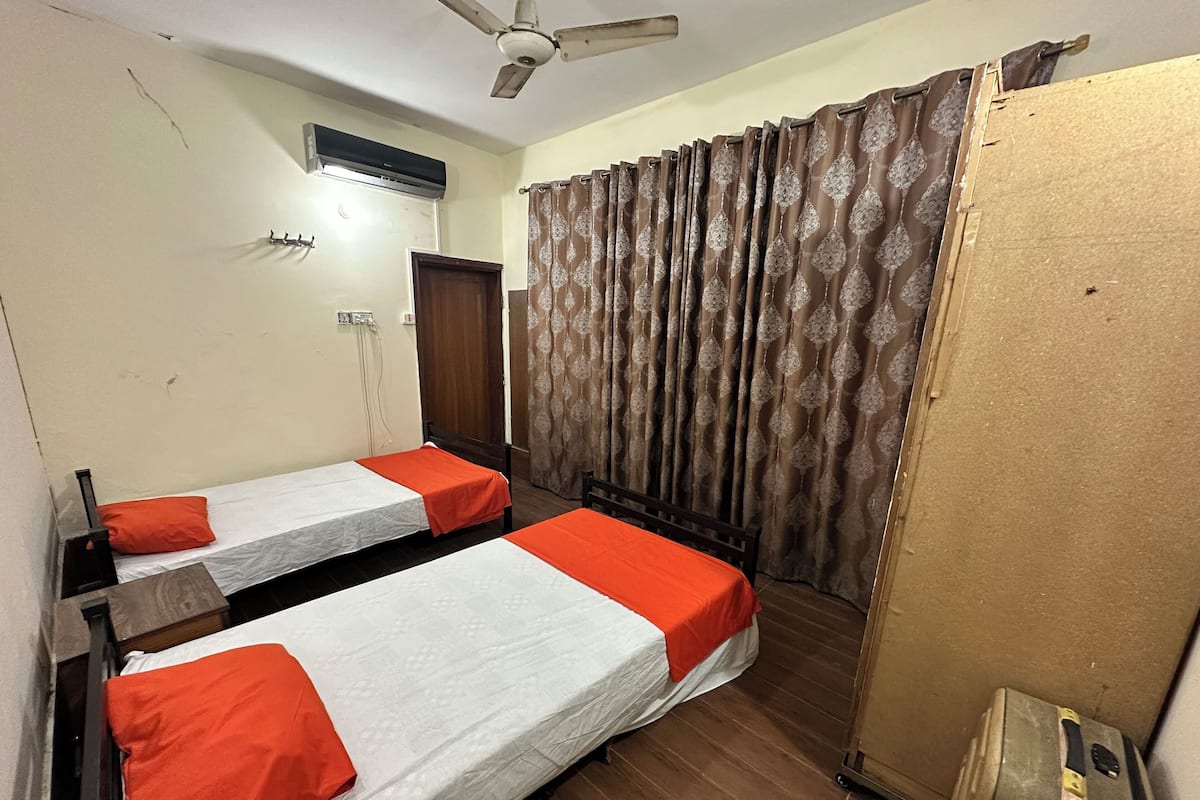 A room with two beds, a ceiling fan, an air conditioning unit, and a curtain.