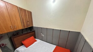 A small, single-bed room with a wooden headboard, a white and orange bedspread, and a wooden wardrobe. - Professional Lahore Hostels (Lahore)