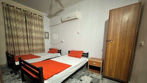 A room with two beds, a wooden wardrobe, a small wooden nightstand, an air conditioning unit, and patterned curtains. - Professional Lahore Hostels (Lahore)