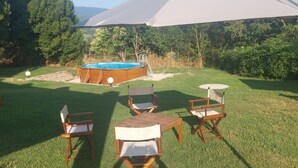 Un espacio al aire libre con mesas y sillas de madera, un jacuzzi y un paraguas grande que proporciona sombra.