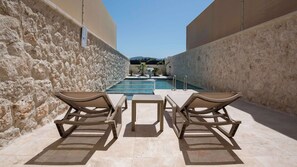 A poolside area with two lounge chairs and a small table, surrounded by stone walls.