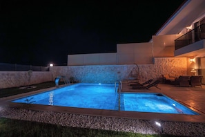 A swimming pool with a waterfall feature, surrounded by a stone wall and a patio area with outdoor furniture.