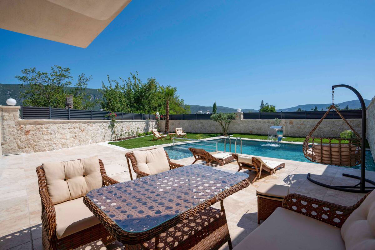 A poolside area with wicker furniture, a glass table, and a hanging chair.