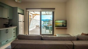 En moderne stue med sofa, fjernsyn og skydedør, der fører til en udendørs patio med swimmingpool og siddeplads.