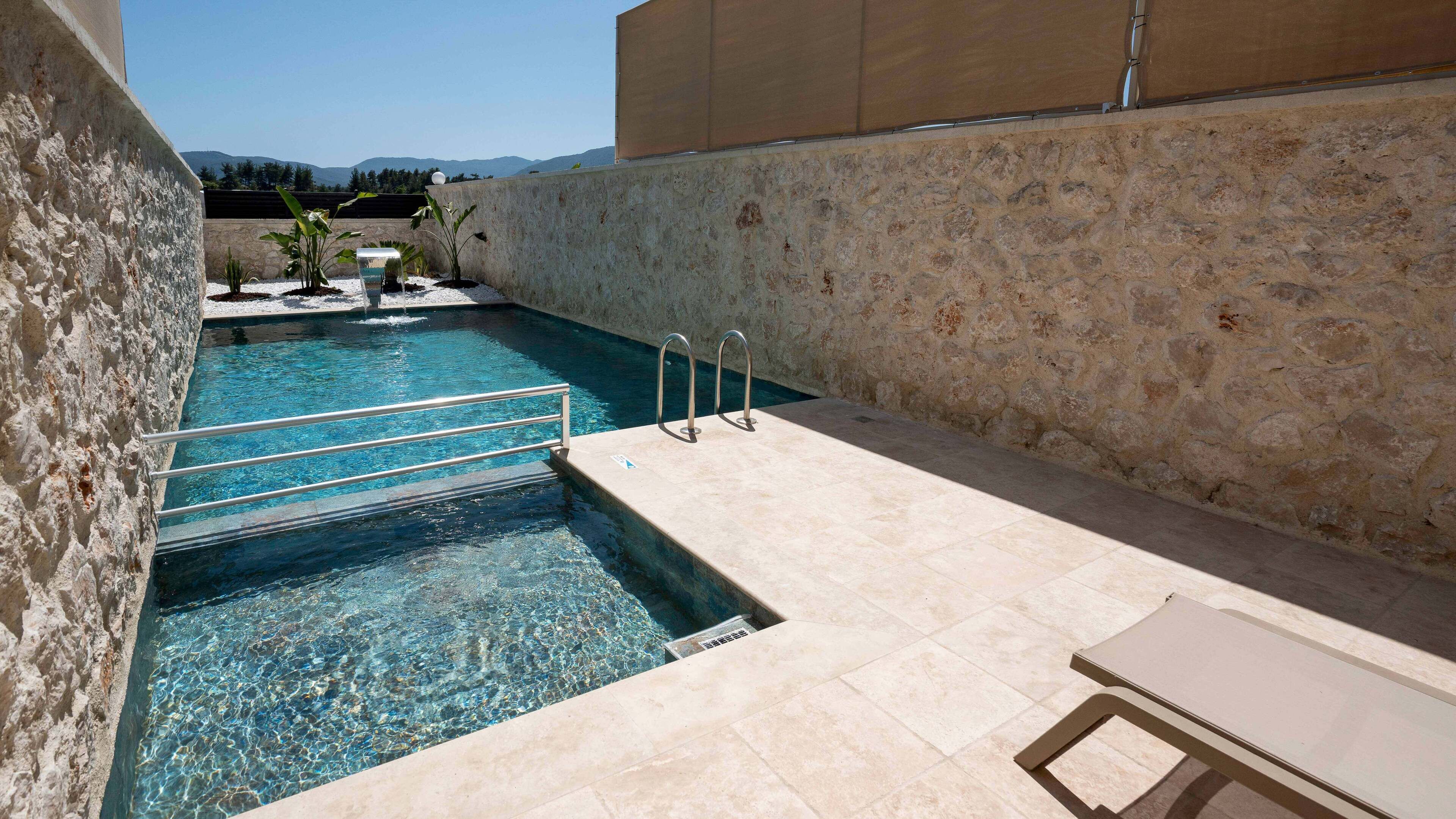 A clear swimming pool with a stone wall and a metal ladder.
