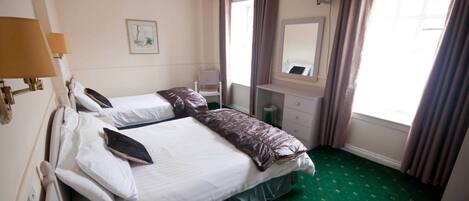 A hotel room with two beds, a desk with a chair, a television, a window with curtains, and a green carpet.