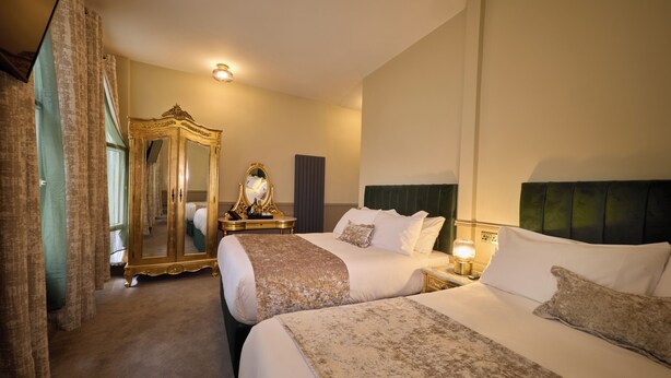 Habitación de hotel con dos camas, un espejo grande, un aparador y una mesita de noche con lámpara.