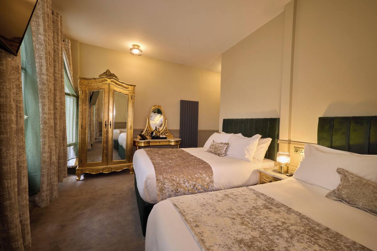 A hotel room with two beds, a large mirror, a dresser, and a nightstand with a lamp.