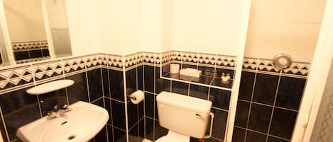 A bathroom with a white sink, toilet, and shower. The walls have black tiles with white patterns.