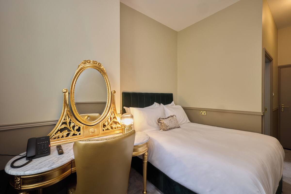 A hotel room with a large bed, a vanity with a mirror, a telephone, and a lamp.