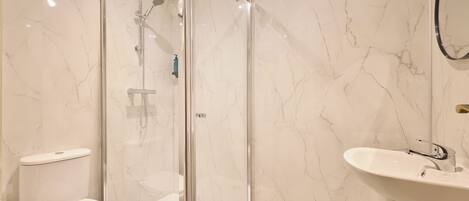 A modern bathroom with a glass-enclosed shower, a white toilet, and a sink with a mirror.