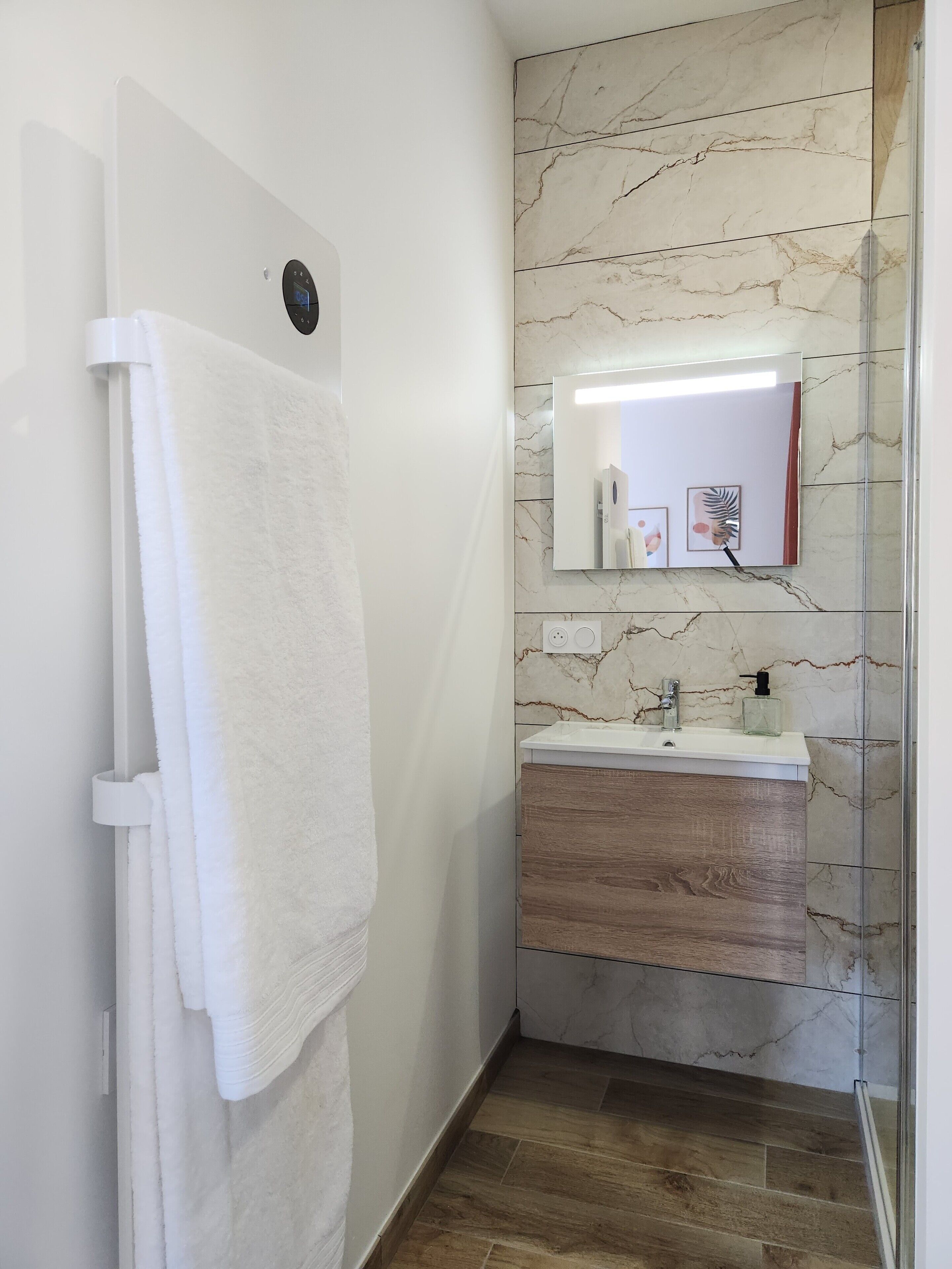 Un baño con una toalla blanca colgada en un perchero, una pared de mármol, un tocador de madera con un espejo y una zona de ducha.