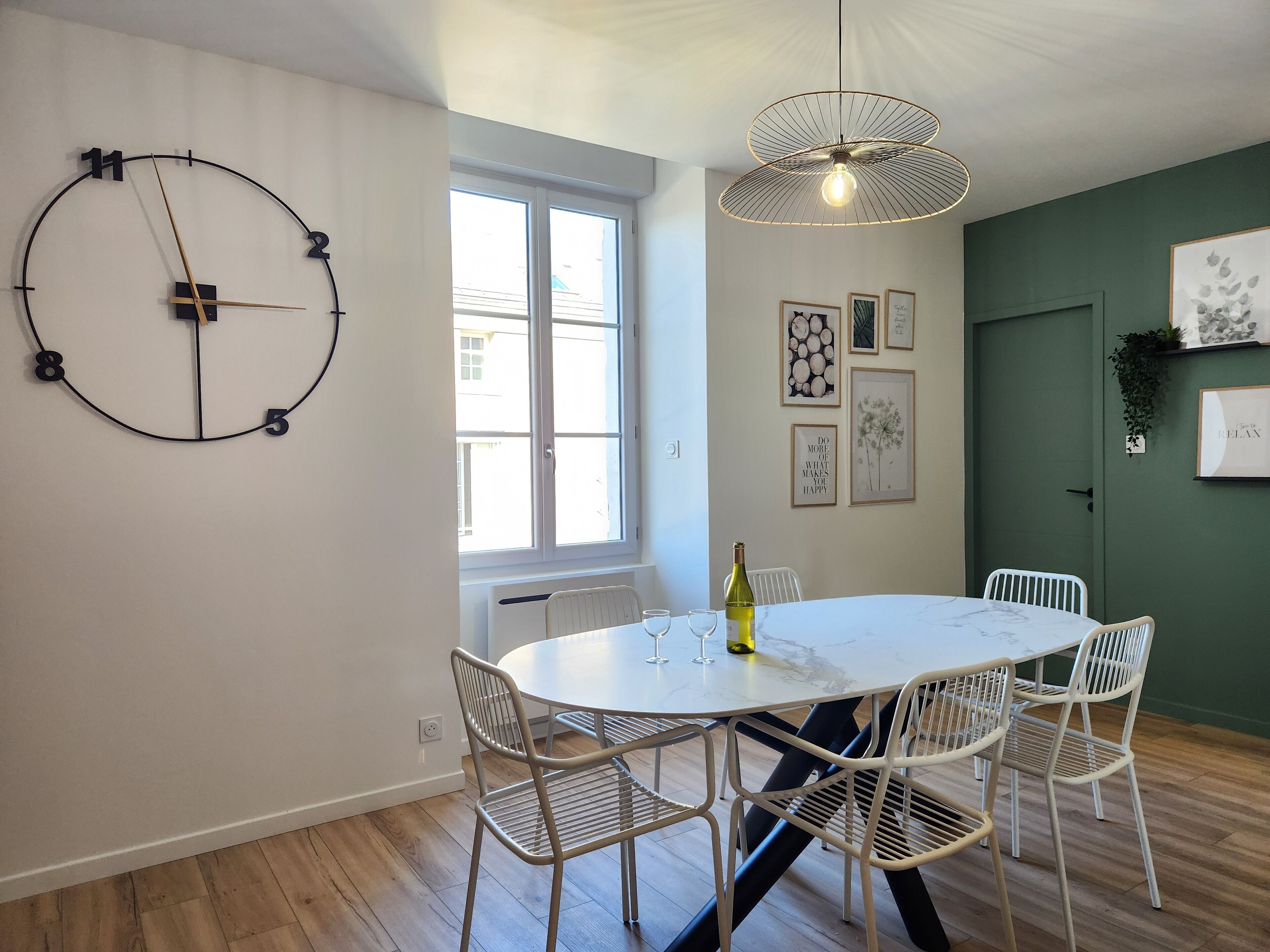 A dining area with a round table, white chairs, a wall clock, and framed artwork.