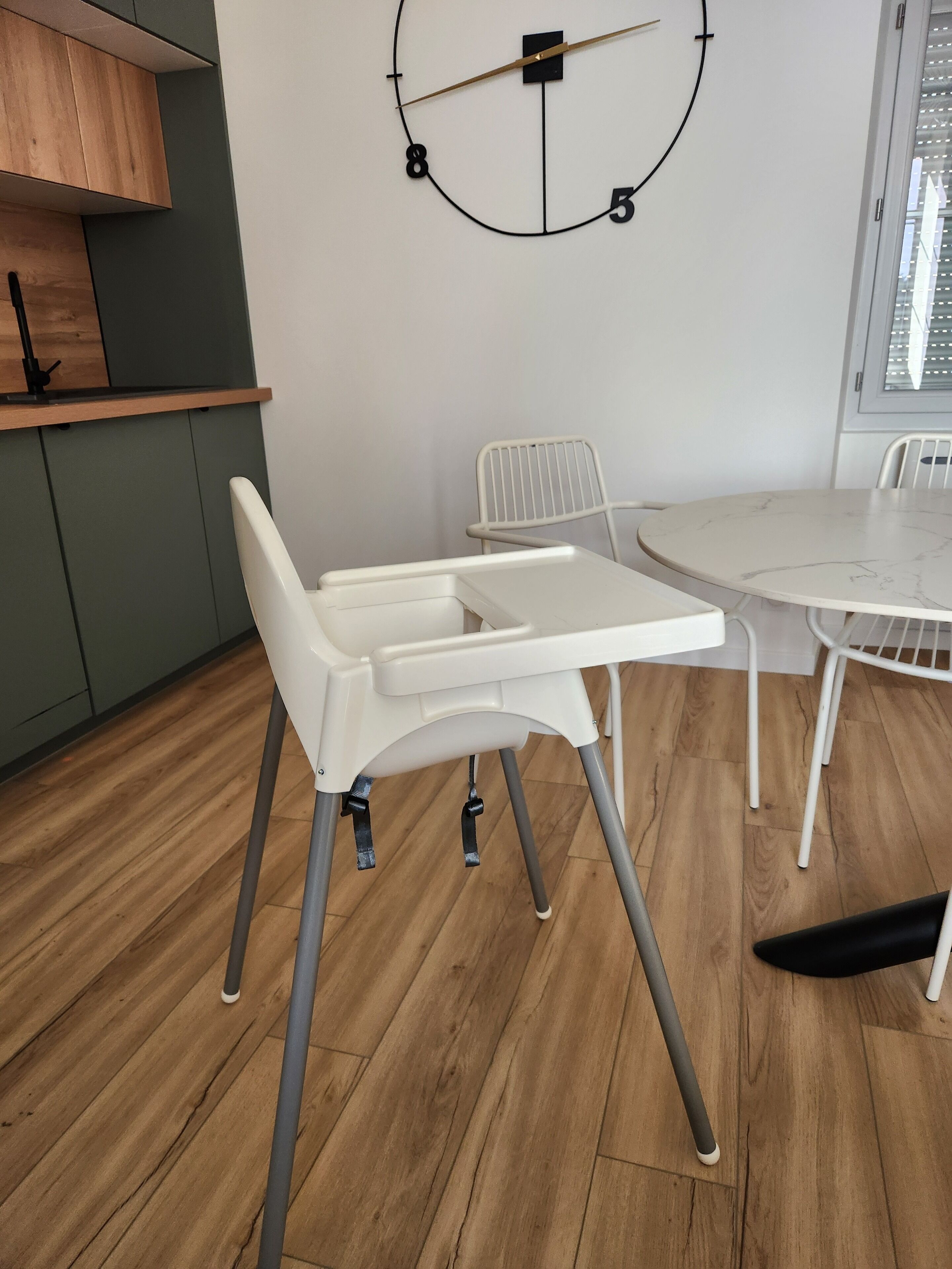 Une cuisine moderne avec une table blanche, des chaises et une horloge au mur.