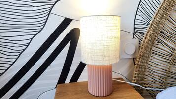 A lamp on a wooden nightstand with a textured lampshade, set against a wall with a black and white abstract design.