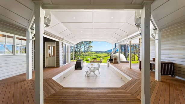 A covered patio with a view of a green landscape, a table with chairs, and a barbecue grill.