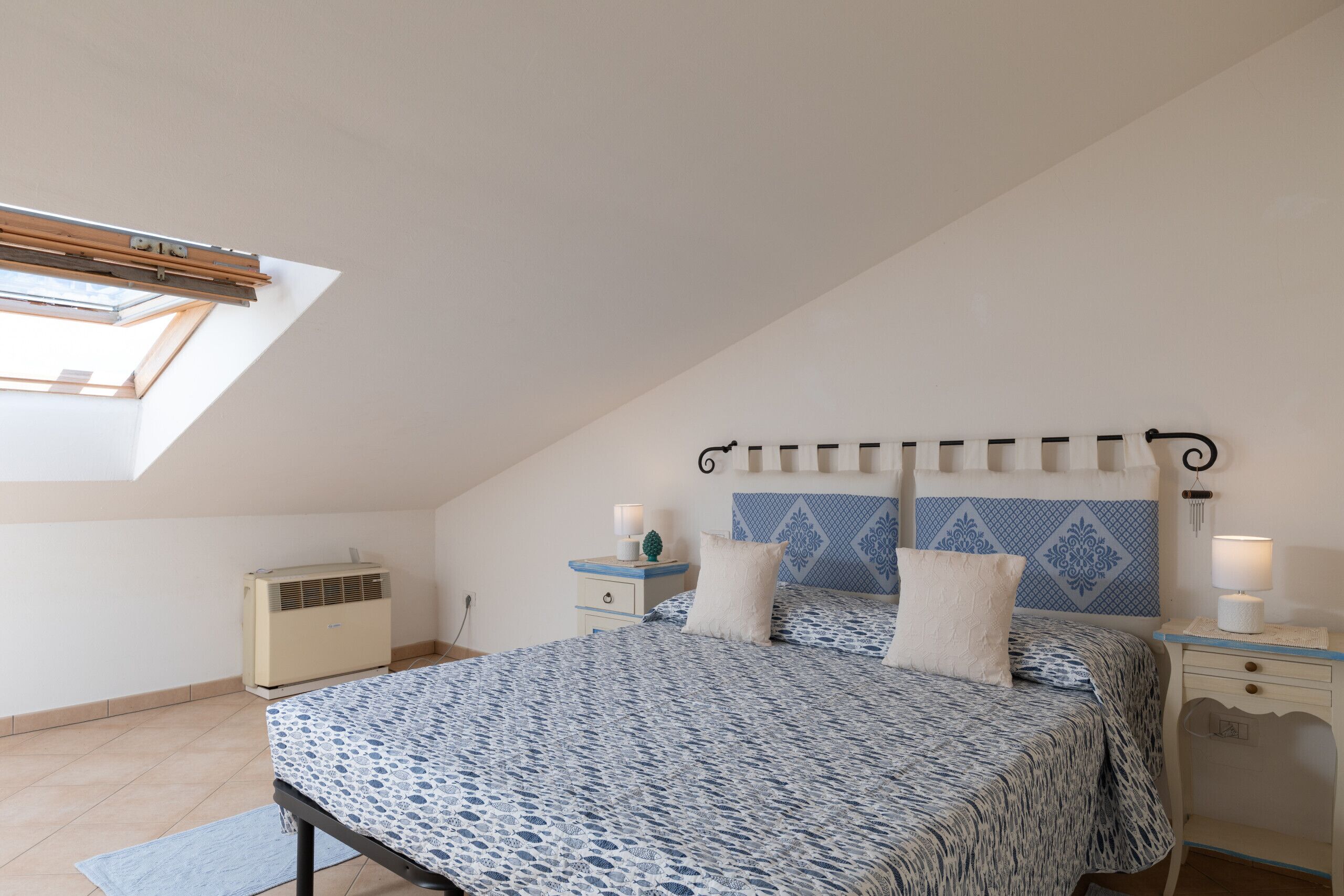 Een slaapkamer met dakraam, een bed met beddengoed met patroon, nachtkastjes met lampen en een decoratief hoofdeinde.