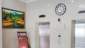 A lobby with two elevators, a clock, and a poster on the wall. - Hotel My All Padang (Padang)